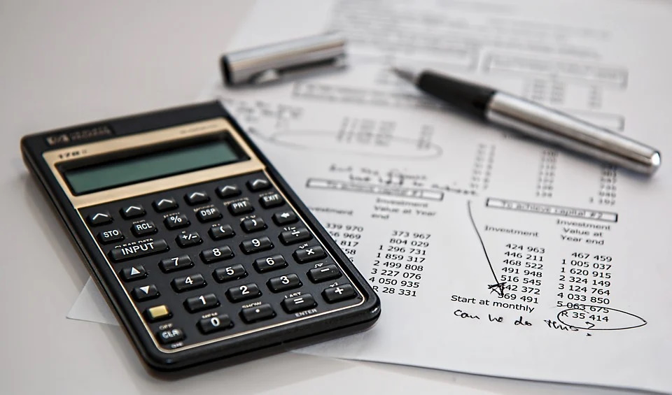 A calculator, a pen, and several other stationary financial objects sitting atop a desk