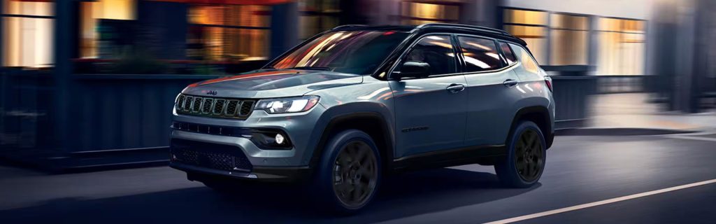 A silver Jeep Compass driving through a city at night with motion blur.