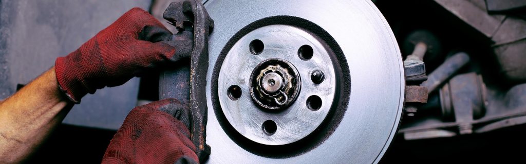 Mechanic in red gloves repairing a car's disc brake assembly.